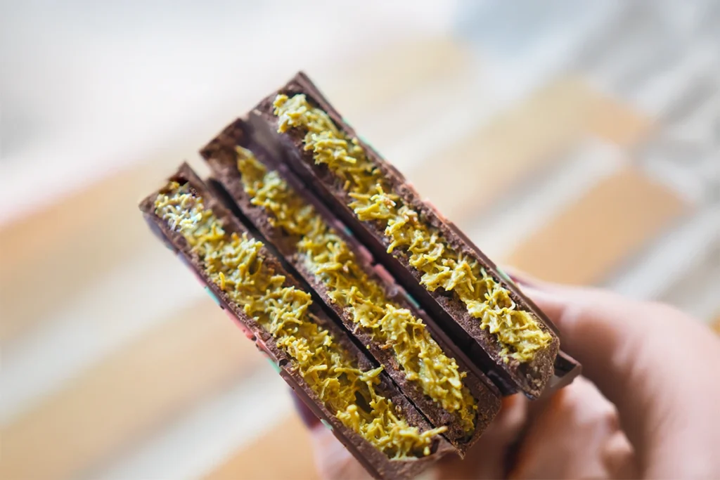 Close-up of a person holding three chocolate bars filled with a golden saffron-infused filling.How to get famous Dubai chocolate