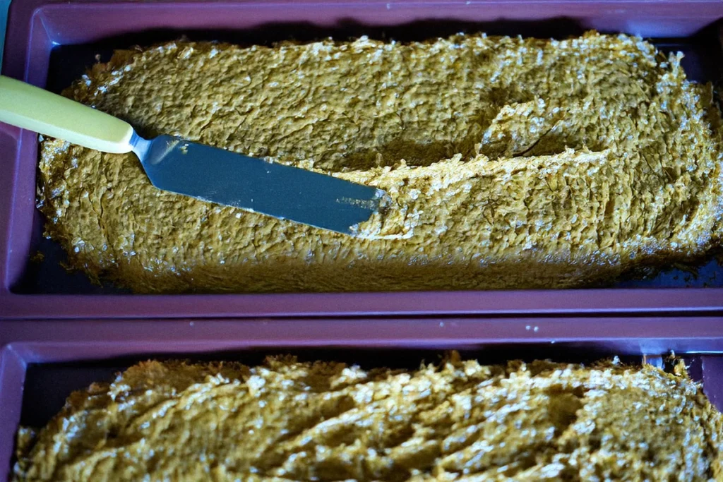 A baking tray filled with pistachio batter being smoothed with a spatula.